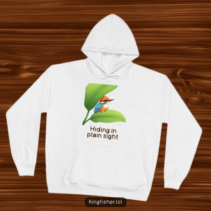 Funny Kingfisher Hoodie: A shy kingfisher peeking from behind a large leaf, depicted on a soft hoodie for funny, relaxed vibes.